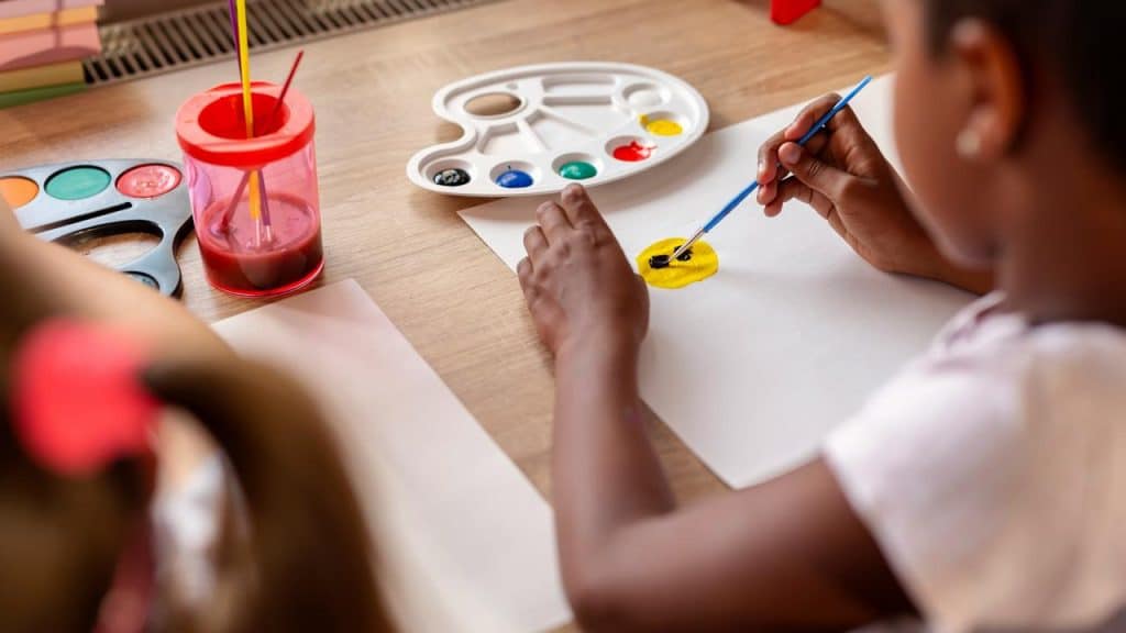 A child painting a yellow circle on white paper at a table.