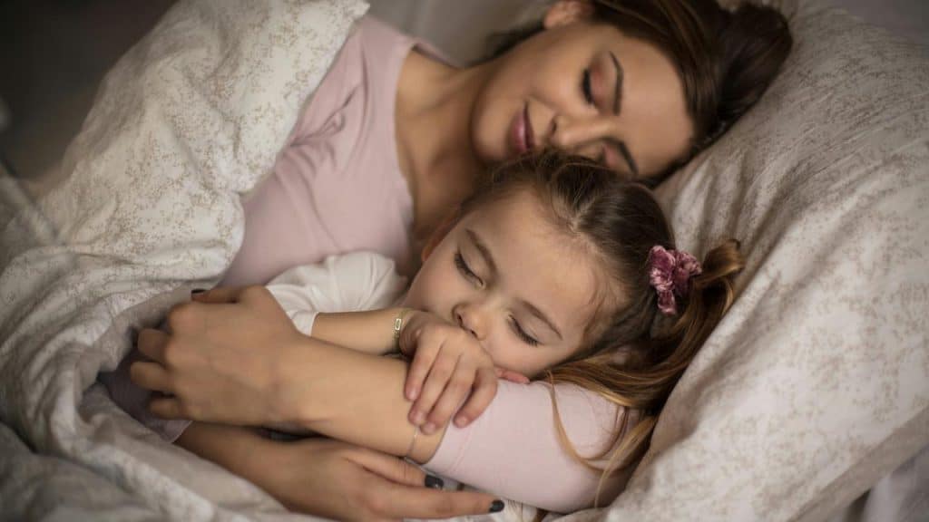 A mother cuddling her sleeping daughter in bed.