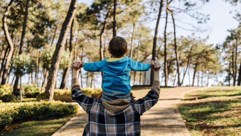 A man carrying a child on his shoulders while walking in a park.