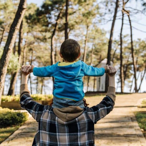 A man carrying a child on his shoulders while walking in a park.