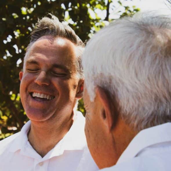 A man smiling while talking to someone outdoors.