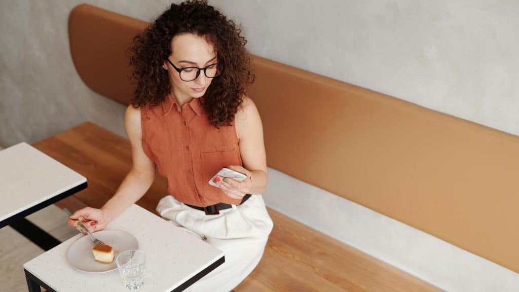A woman looking at her phone while eating cake.