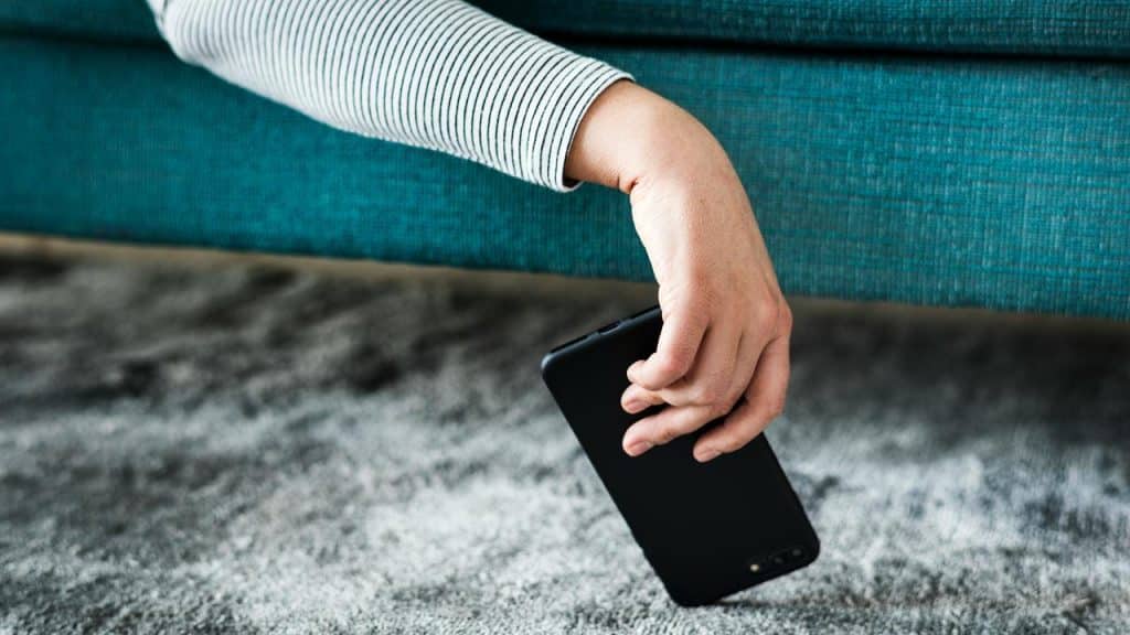 A person's hand holding a smartphone as they lay on a couch.