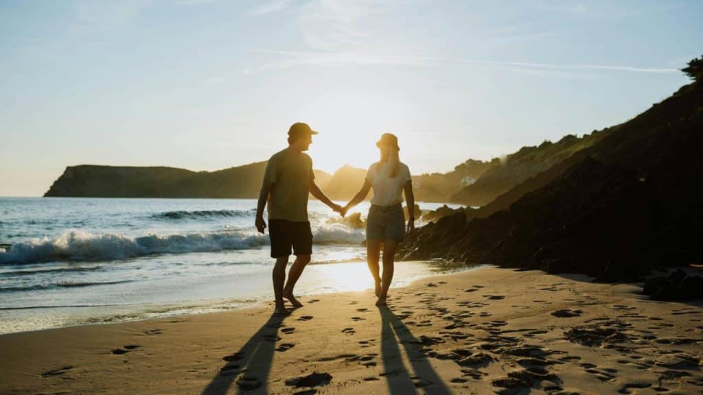 A couple holding hands while walking on a beach.