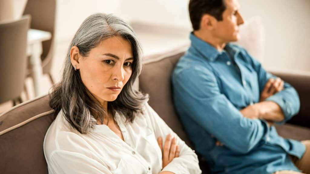 A displeased woman with her arms crossed sits on a couch next to a man looking away.