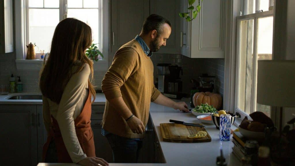 A man is cooking in a kitchen while a woman stands nearby, looking at him.