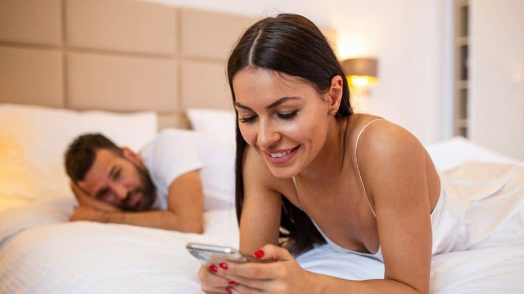 A woman smiling while on her phone, with a man looking on from behind.