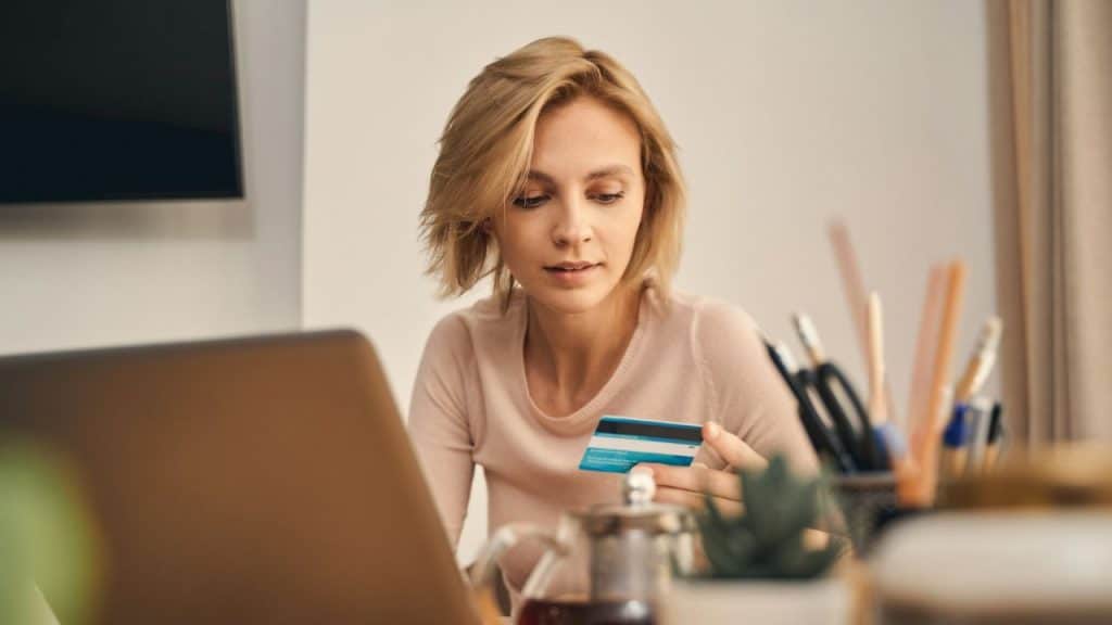 A woman looks intently at her laptop, holding a credit card.