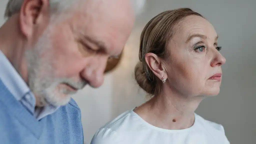 A focused elderly woman is sitting next to a man, who is looking down.