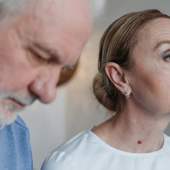 A focused elderly woman is sitting next to a man, who is looking down.