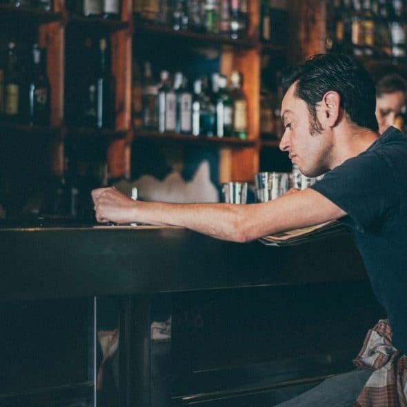 A sad-looking man is slumped over a bar in a dimly lit room.