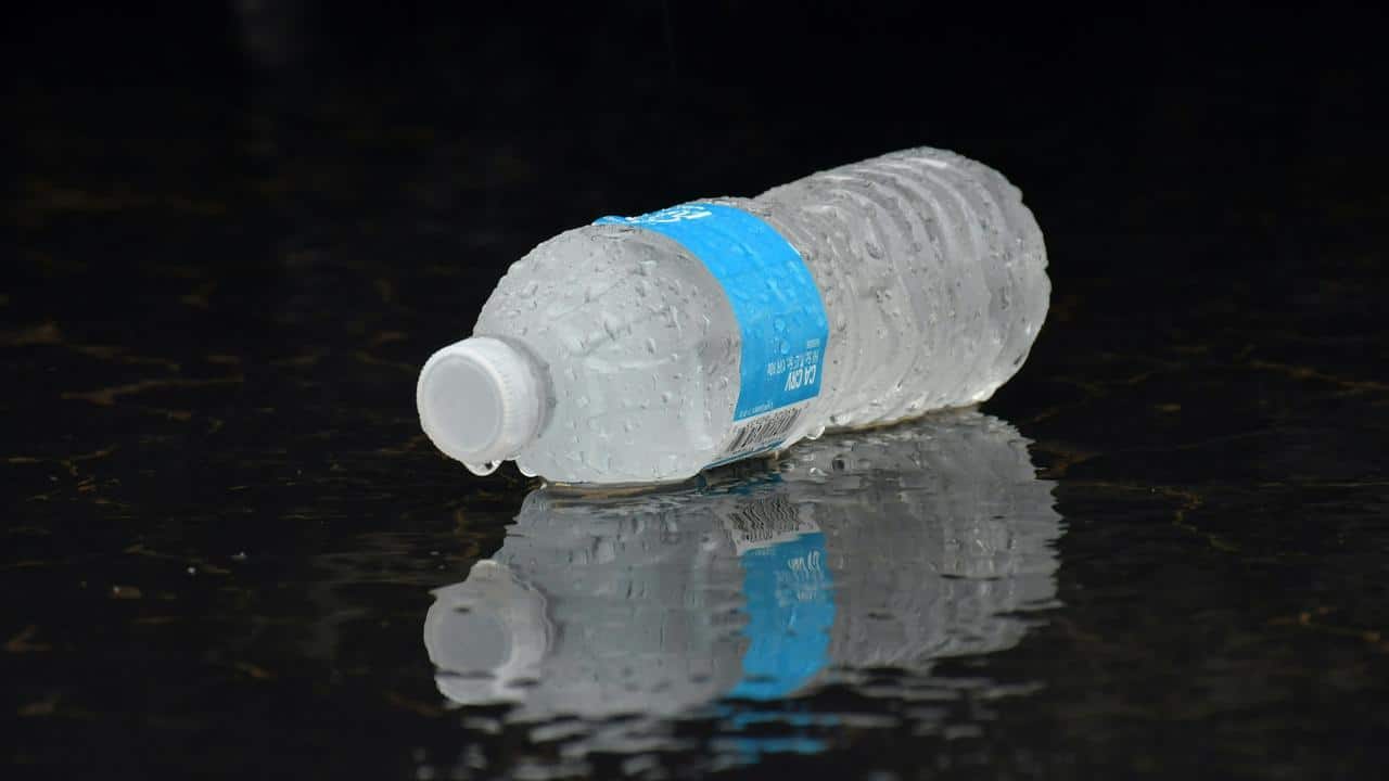 A wet plastic water bottle with a blue label lying on a reflective surface.