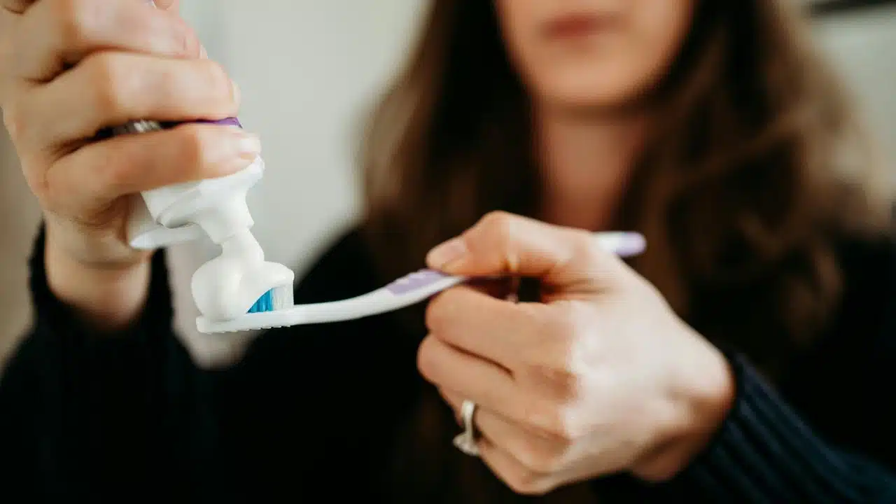 A person squeezing toothpaste onto a toothbrush.