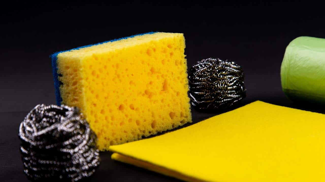 A yellow sponge next to metal scrubbers and a trash bag roll.