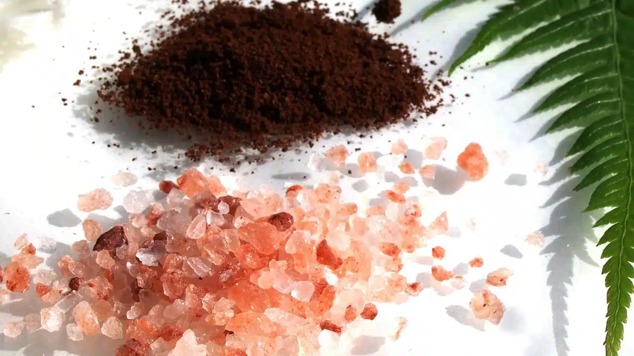 A pile of ground coffee and pink Himalayan salt crystals.