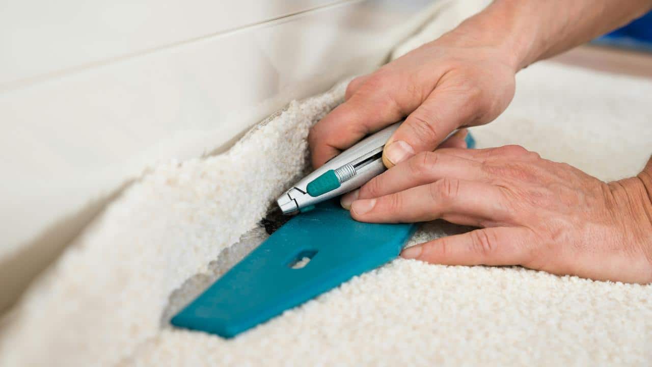 A person cutting carpet along a wall with a utility knife.