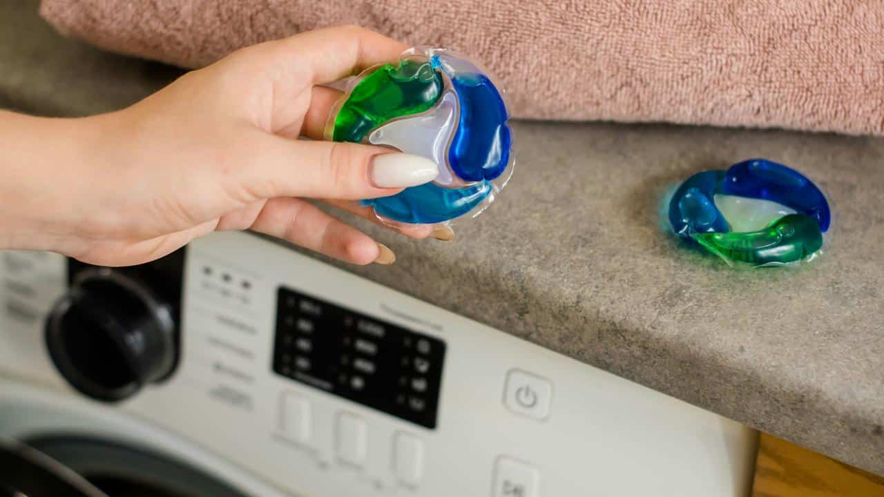 A person holding a laundry detergent pod above a washing machine.