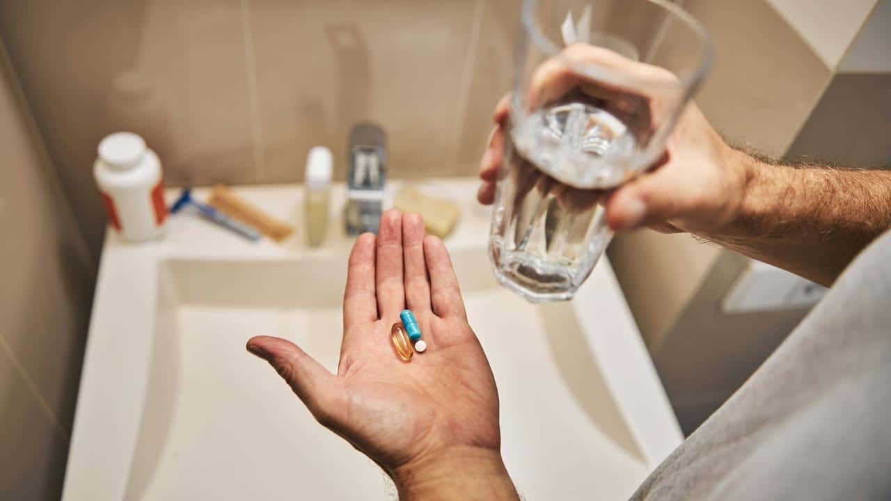 A person holding pills in one hand and a glass of water in the other.