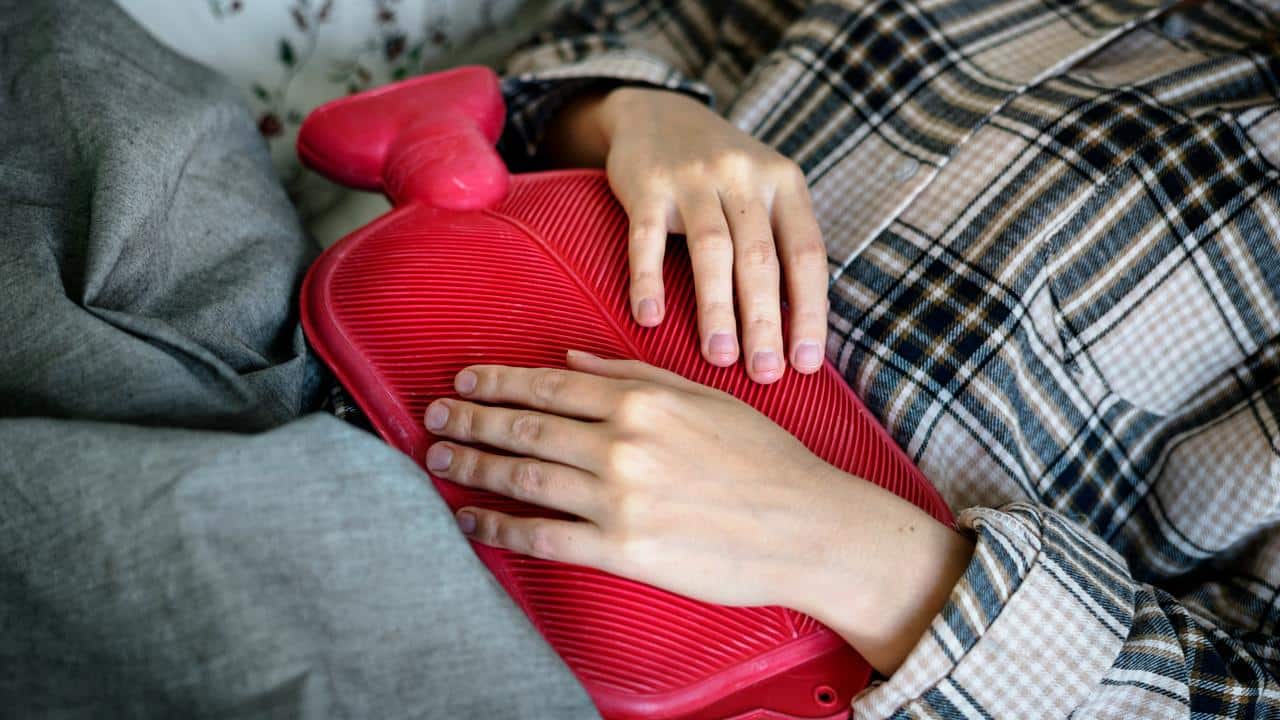 A person holding a red hot water bottle on their stomach.