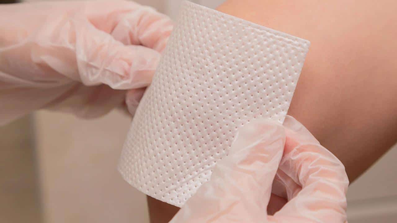 A person applying a large adhesive bandage to someone’s arm.