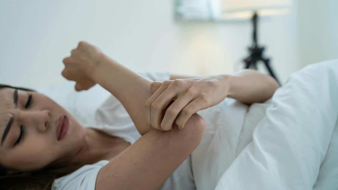 A woman scratching her arm while lying in bed.