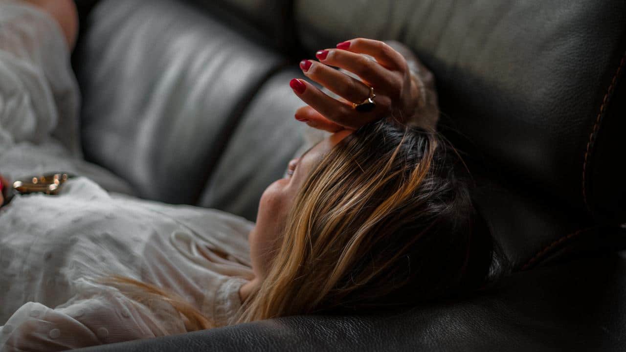 A woman lying on a couch with her hand on her forehead.