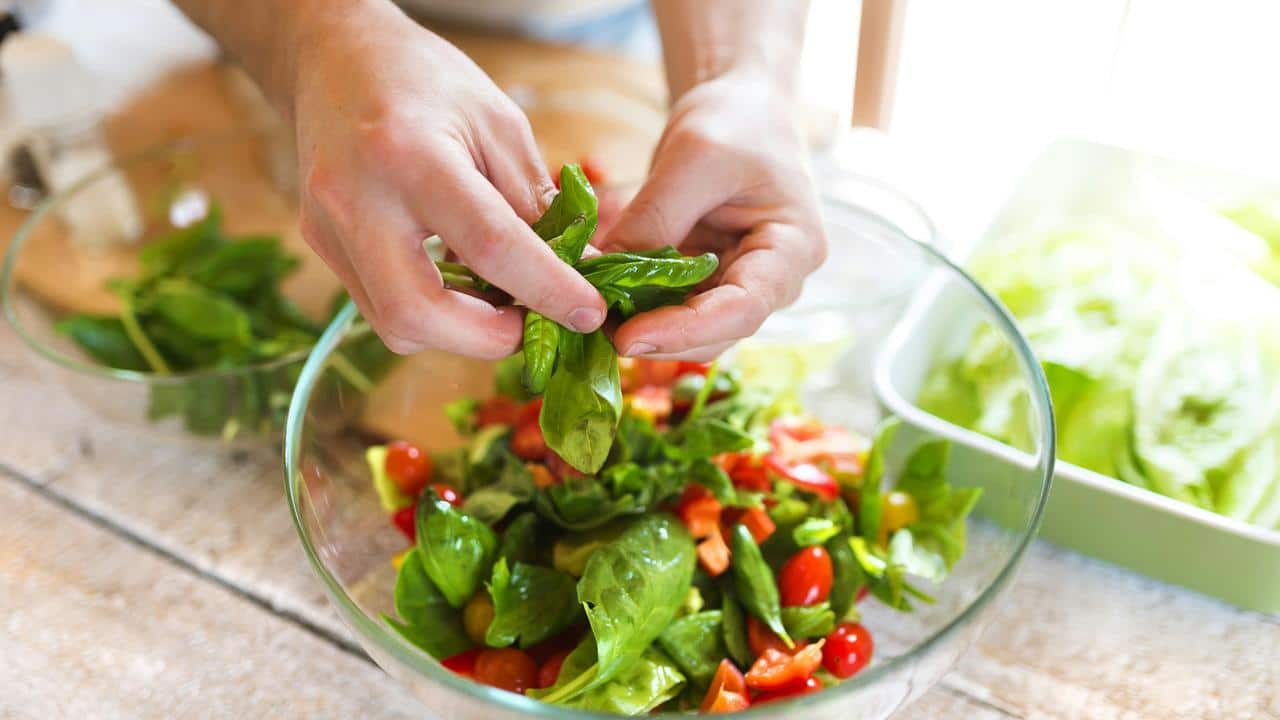 A person preparing a salad with spinach, cherry tomatoes, and red bell peppers.