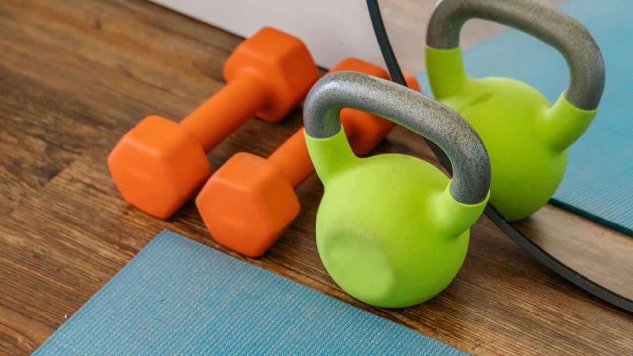 A set of orange dumbbells and a green kettlebell on a yoga mat.