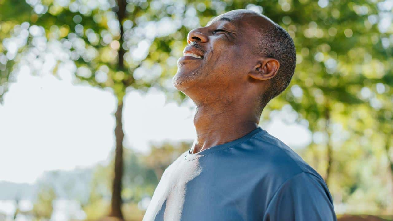 A man enjoying fresh air outdoors with eyes closed and a smile.