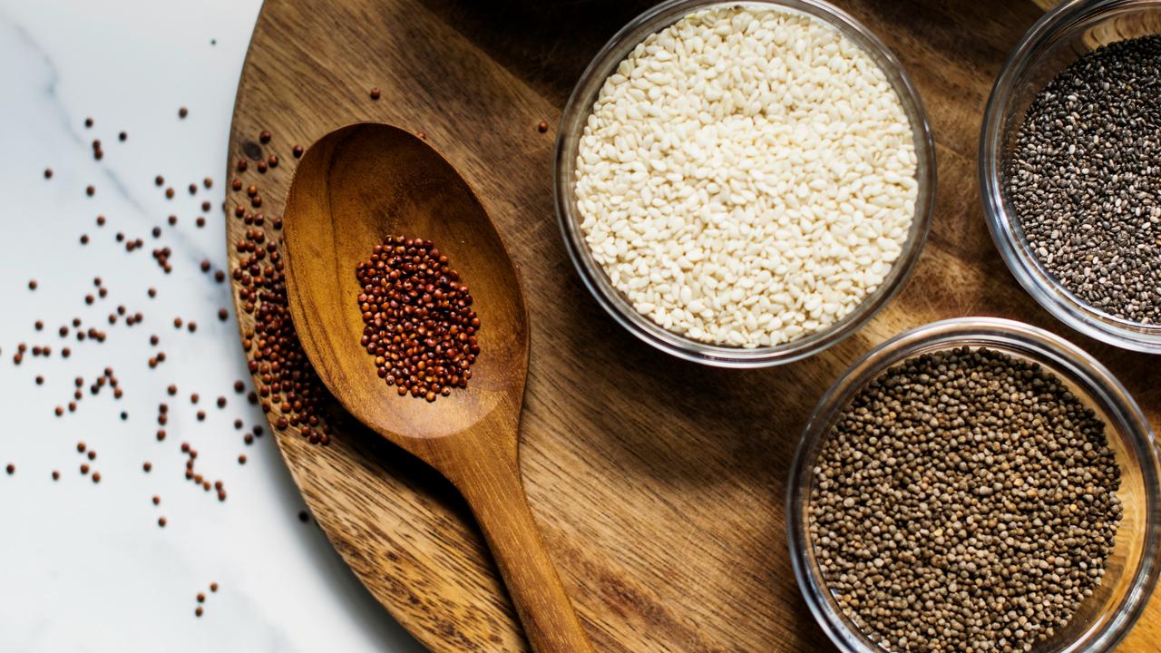 A wooden spoon and bowls of assorted seeds.