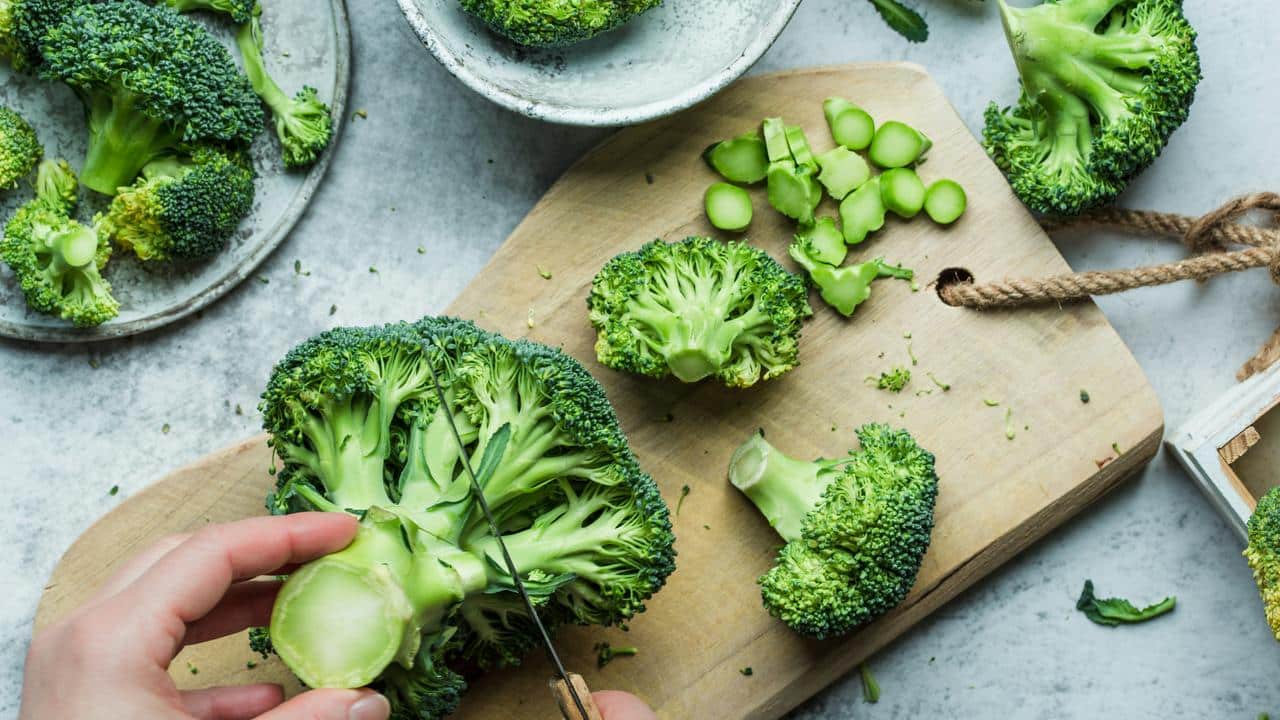 A person cutting fresh broccoli on a wooden board.