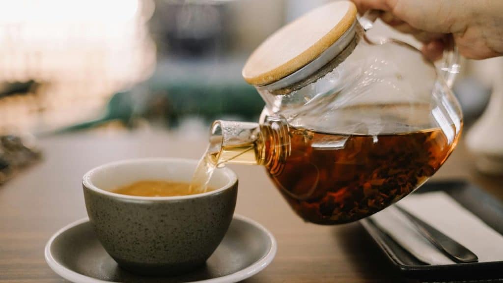 A glass teapot pouring tea into a gray cup.