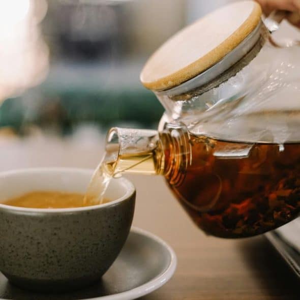 A glass teapot pouring tea into a gray cup.