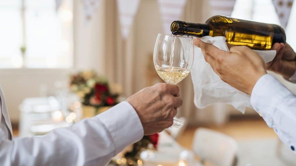 A bottle of white wine being poured into a glass.