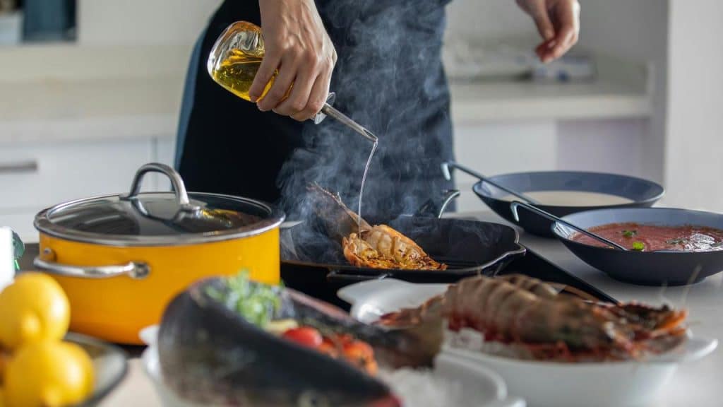 An individual cooking seafood and drizzling oil into a hot pan.