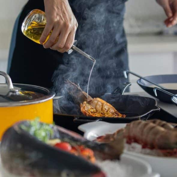 An individual cooking seafood and drizzling oil into a hot pan.