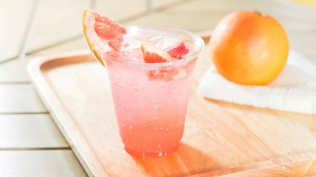A refreshing pink grapefruit soda with ice and citrus slices.