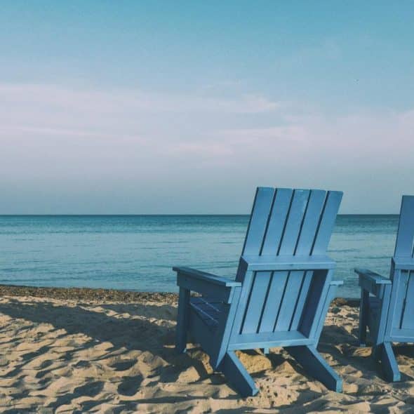 A pair of blue chairs on a sandy beach facing the sea.