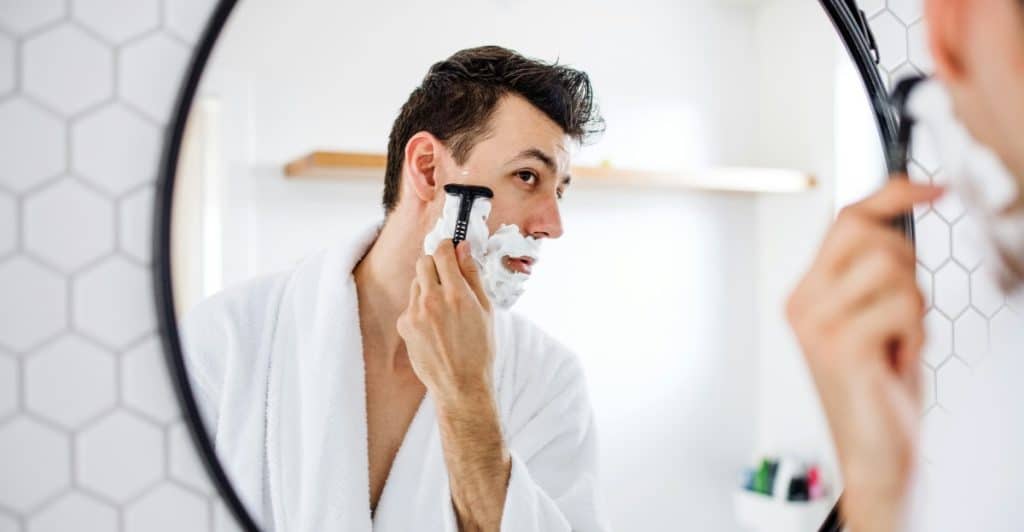 Man shaving beard in bathroom mirror