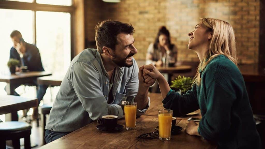 A happy couple is holding hands and laughing across a cafe table.