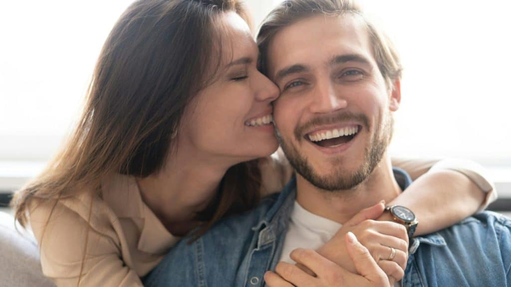 A laughing couple embraces, with the woman affectionately nuzzling the man's cheek.