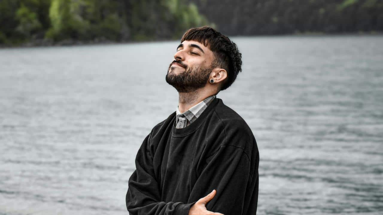 A person standing by the water with eyes closed.
