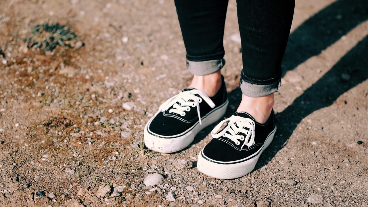 A person wearing black sneakers on a dirt path.