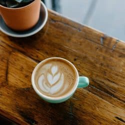 A cup of latte with heart-shaped latte art on a wooden table.