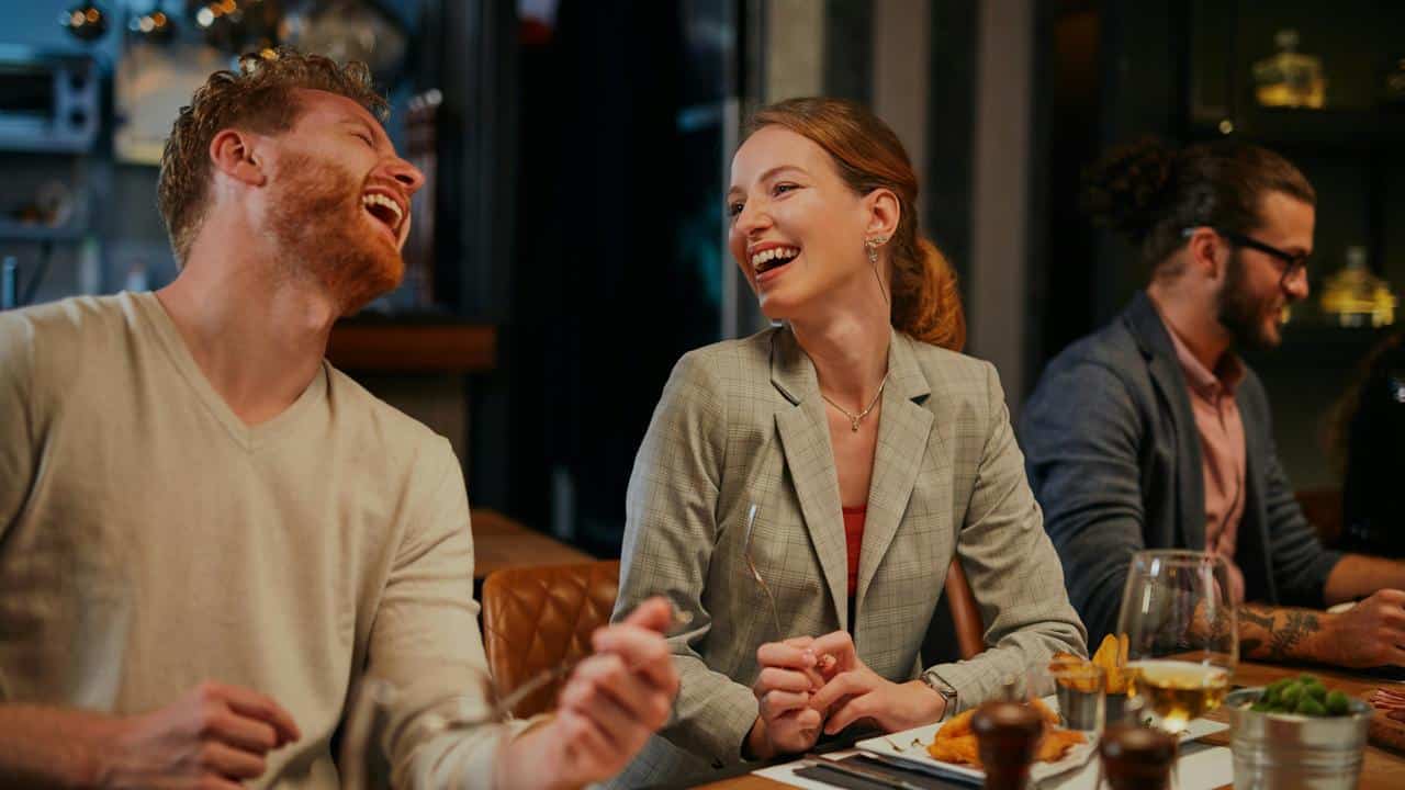 A man and woman laughing together while dining at a restaurant.
