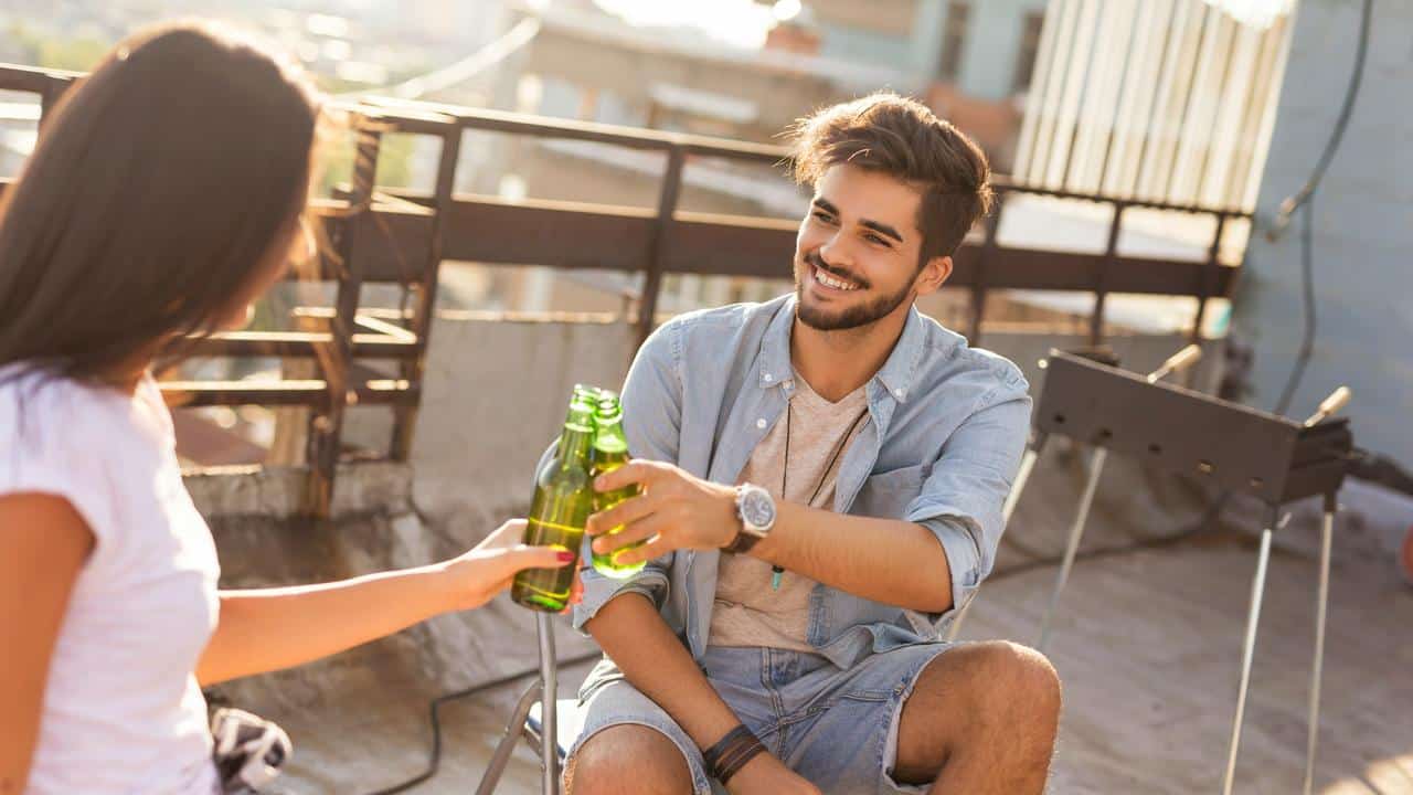 A man and woman clinking beer bottles on a rooftop.