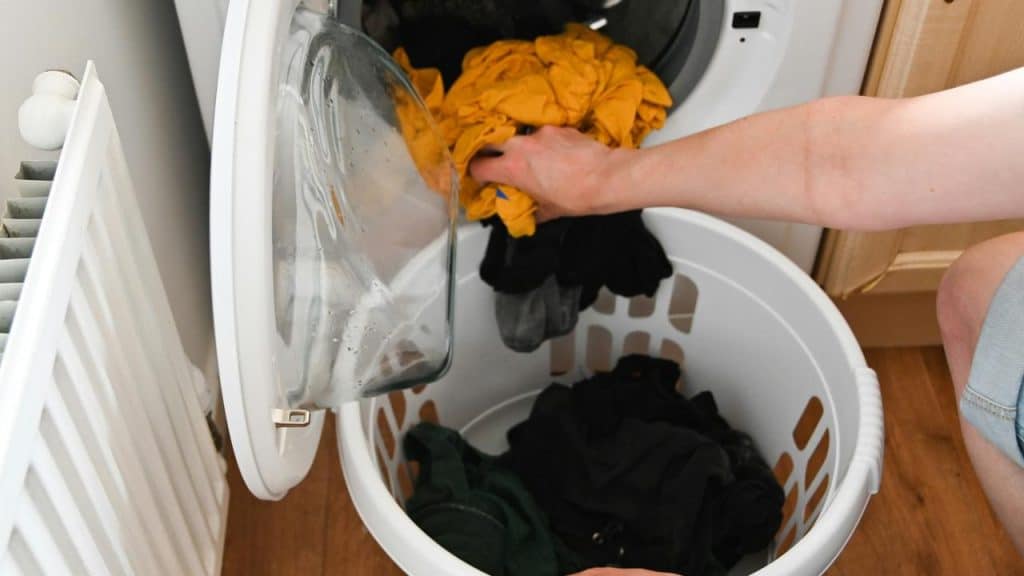 A person transferring clothes from a washing machine to a laundry hamper.