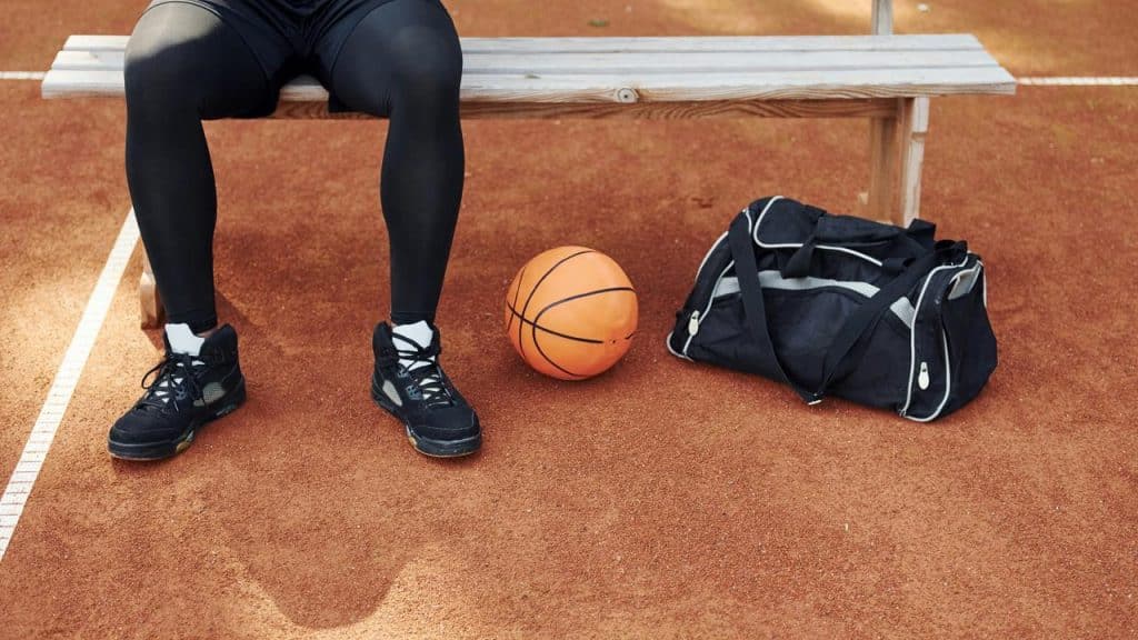 A photo of a person’s lower limbs next to a basketball and gym bag.