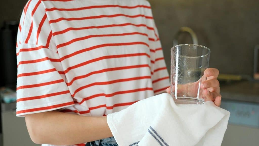 A person wiping the bottom of a water glass with a dish towel.