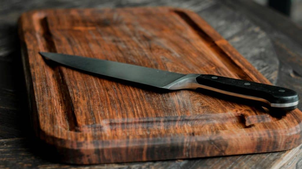 A wooden cutting board with a chef’s knife resting on top.